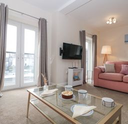 A living room with pink sofas a glass coffee table a wall mounted television and french doors at Weydale Avenue in Scarborough
