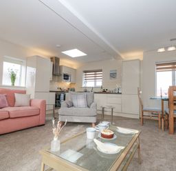An open plan living room and kitchen with pink sofas a grey armchair a glass coffee table with cups and cake and a wooden dining table with chairs at Weydale Avenue in Scarborough