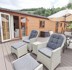 An outdoor deck with two armchairs and footrests a dining table with chairs and a large umbrella at Esthwaite Lodge Beckside 43 Limefitt Park near Windermere