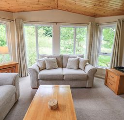 A living room with sofa armchairs wooden coffee table side tables and large windows at Esthwaite Lodge Beckside 43 Limefitt Park near Windermere