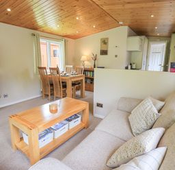 A living room with a beige sofa wooden coffee table dining table with chairs and a television on the wall at Esthwaite Lodge Beckside 43 Limefitt Park near Windermere