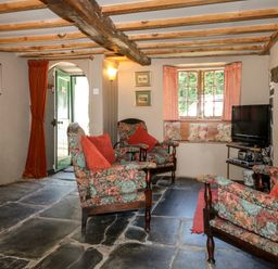 A living room with floral armchairs red cushions stone floor and a television at Bell Buoy Cottage in Morwenstow