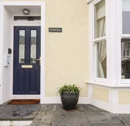 A front door with a dark blue door and glass panels next to a window and a plant pot on a stone porch at Hyfrydle in Borth-Y-Gest