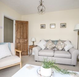 A living room with a sofa with cushions an armchair a wooden door and a coffee table with a plant at Hyfrydle in Borth-Y-Gest
