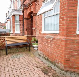 A small paved front yard with a wooden bench and potted plants outside a red brick house at Ellan Vannin in Sheringham