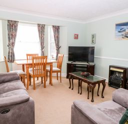 A living room with a dining table and chairs a television on a stand and two sofas at Ellan Vannin in Sheringham