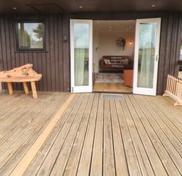 A wooden deck with a natural wood bench outside doors leading to a living room at 3 Valley View Lodges in Nawton near Helmsley