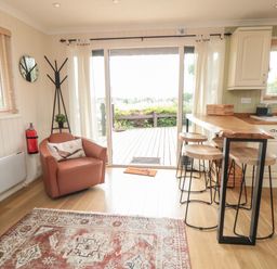A living area with a leather chair a wooden high table with stools a rug and sliding glass doors at 3 Valley View Lodges Nawton near Helmsley