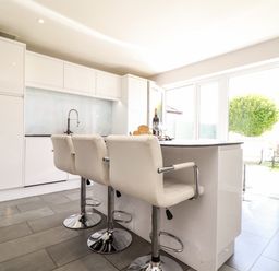A modern kitchen with a white island and three white bar stools at Summerhayes in Park Bottom