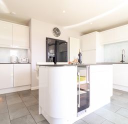 A kitchen with white cabinets a black refrigerator an island with a wine bottle and glasses and a wall clock at Summerhayes in Park Bottom