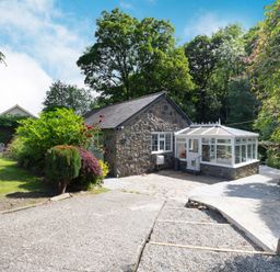 A stone cottage with a glass conservatory surrounded by trees and garden at Nant Cottage in Rowen