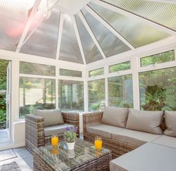 A conservatory with wicker furniture including a sofa and chair a glass table with two glasses of orange juice and a potted plant at Nant Cottage in Rowen