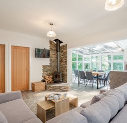 A living room with a gray sofa a wood stove and a dining area in a glass sunroom at Nant Cottage in Rowen