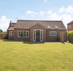 A brick house with a tiled roof and green lawn in front at The Croft in Thompson near Watton