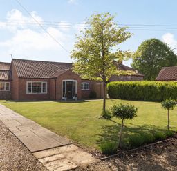 A brick house with a tiled roof a lawn with trees and a paved pathway at The Croft in Thompson near Watton