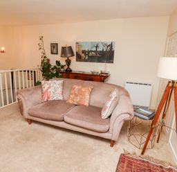 A sitting area with a sofa, cushions, a floor lamp, side table with books, a wooden sideboard with a lamp and plants at Beals Yard in Alnwick