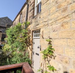 A stone house exterior with a wooden door and climbing plants at Beals Yard in Alnwick