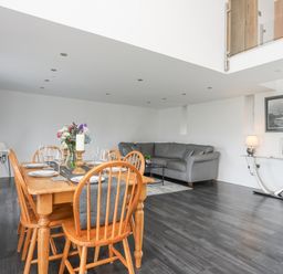 A dining area with a wooden table set with plates and glasses and a gray sofa in the living space at Gwel Y Fenai in Y Felinheli