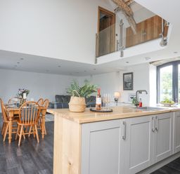 A kitchen island with sink and plants next to a dining table with wooden chairs and a living area with a sofa at Gwel Y Fenai in Y Felinheli