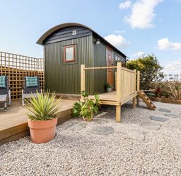 A small cabin with a wooden deck surrounded by gravel and potted plants at Badgers Rest in Tintagel