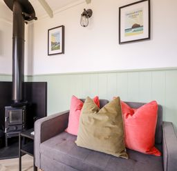 A corner with a wood-burning stove and a gray sofa with colored cushions at Badgers Rest in Tintagel