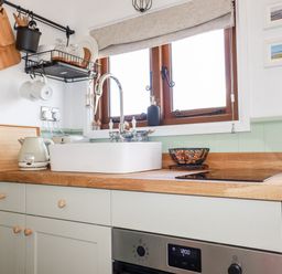 A kitchen countertop with a sink kettle cutting boards and a fruit basket at Badgers Rest in Tintagel