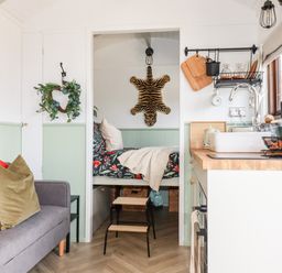 A small living area with a grey sofa and cushions next to a kitchen with a sink and wooden countertop at Badgers Rest in Tintagel