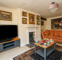 A living room with a television on a stand a fireplace a sofa a coffee table with cups and fruit and paintings on the walls at The Town House in Dorchester
