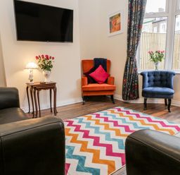A living room with a wall-mounted TV colorful zigzag rug two armchairs and a sofa at Harbour Hideaway in Whitby