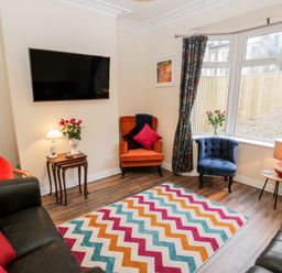 A living room with colorful chairs a zigzag patterned rug and a wall-mounted TV at Harbour Hideaway in Whitby