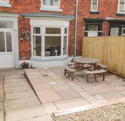 A patio area with a round wooden table and benches outside a red brick house at Harbour Hideaway in Whitby
