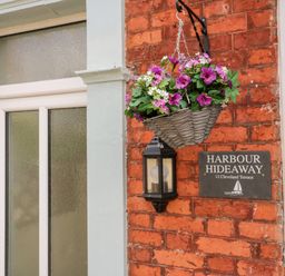 A hanging basket of flowers beside a light and a sign on a brick wall at Harbour Hideaway in Whitby