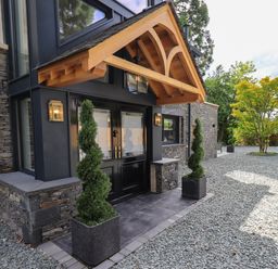 The front entrance of a house with double black doors stone walls wooden porch and spiral topiary plants in pots at Hares Breath in Bowness-On-Windermere
