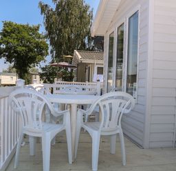 An outdoor deck with white plastic table and chairs attached to a mobile home at The Goodwood Lodge in Runcton near Chichester