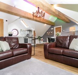 A living room with two brown leather sofas and green pillows open to a kitchen and dining area at The Coach House in Ludlow