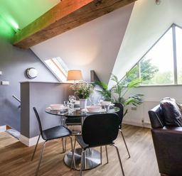 A dining area with a glass table set for four and black chairs next to a window and a brown leather sofa in a room at The Coach House in Ludlow