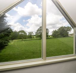 A triangular window showing a green field with trees under a cloudy sky at The Coach House in Ludlow