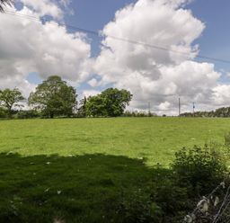 A green field with trees and a wire fence under a cloudy sky at The Coach House in Ludlow