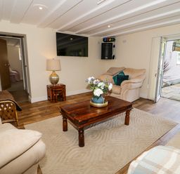 A living room with sofas a wooden coffee table flowers on table lamp on side table and open doors to garden at Plas Eithin in Mynydd Mechell near Llanfechell