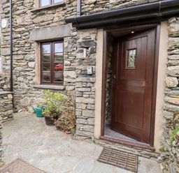 The entrance to a stone house with a wooden door and a window next to it at The Curious Orange in Troutbeck