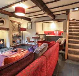 A living room with a red sofa a glass dining table a wood stove and carpeted stairs at The Curious Orange in Troutbeck