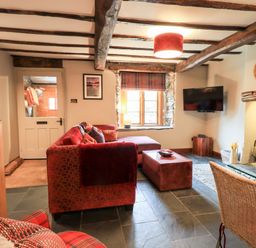 A living room with wooden beams red sofa wood stove and wall mounted tv at The Curious Orange in Troutbeck
