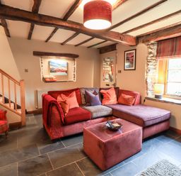 A living room with a sectional sofa table and armchair near a window at The Curious Orange in Troutbeck