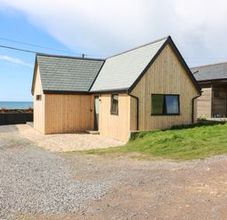 A small wooden house with a gravel driveway near the sea at Sandpiper Chalet in Eype