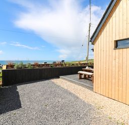An outdoor area with gravel and a wooden patio next to a wooden building overlooking the sea at Sandpiper Chalet in Eype
