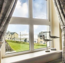 A window with curtains and bird sculptures on the sill overlooking houses and a grassy area at Beach View in Duncannon near Ramsgrange County Wexford