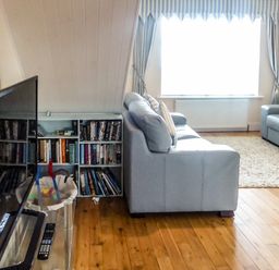 A living room with two sofas a TV on a stand a bookshelf and a window with striped curtains at Beach View in Duncannon near Ramsgrange County Wexford