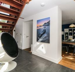 A hallway with a modern round chair and wooden staircase leading up with a dining room in the background at Iroko Millbrook