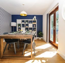 A dining room with a wooden table set for six and a white shelving unit against a blue wall with a patterned wall at Iroko in Millbrook