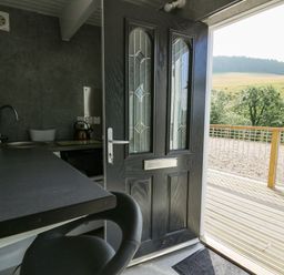 A small kitchen area with a black door open to a wooden deck and countryside view at Caban Glas in Llanafan near Pontrhydfendigaid